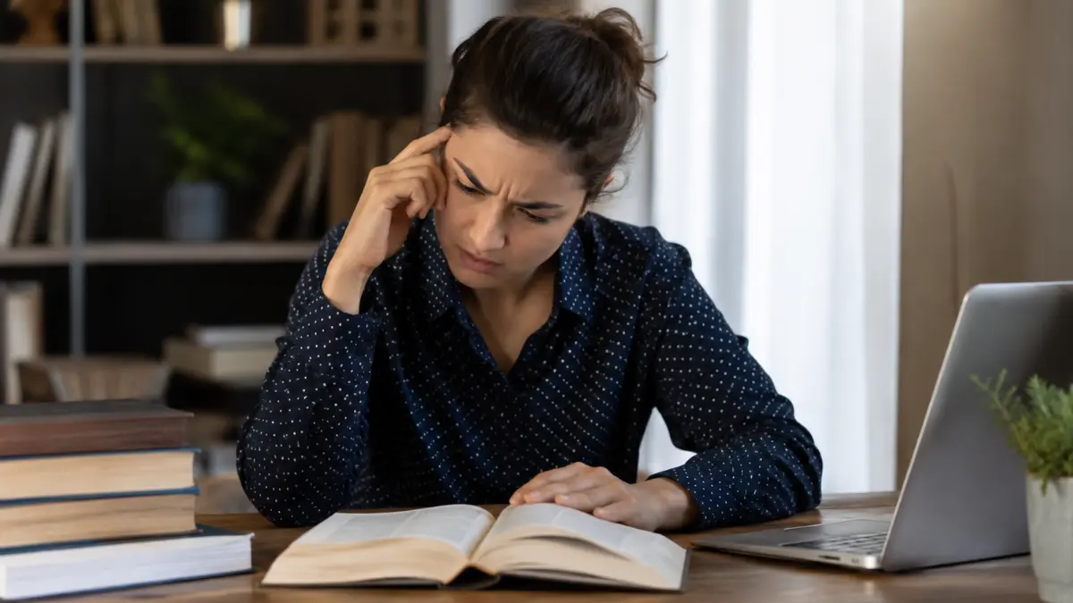 Woman concentrating on an open book while struggling to remember what she has read.
